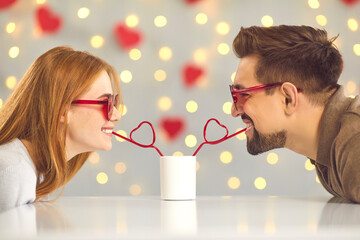Cute happy young couple sipping drink from one cup on their date on Valentine's Day