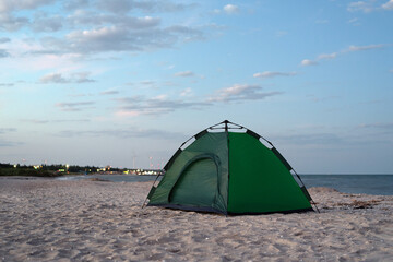 Green tent on the sandy shore against blue sky and sea background. Camping, active tourism