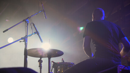 Closeup back view the drummer plays rock on music festival. View from the stage at a European-looking man playing drums, cymbals and percussions.