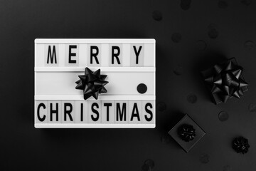 Lightbox with text message Merry Christmas. Traditional black decorative balls on a dark background .Creative Concept for Greeting Holiday Card. Flat lay top view