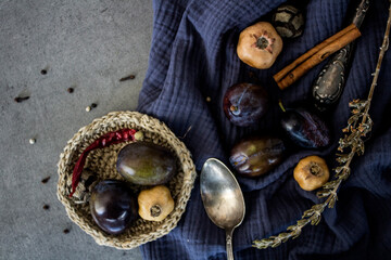 Still life with fresh plums, dry herbs and silver spoon on navy blue fabric. Top view photo of different objects. Colors of August. 