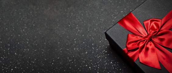 Black gift box with a red ribbon and a large bow on a granite dark background. Place for the inscription