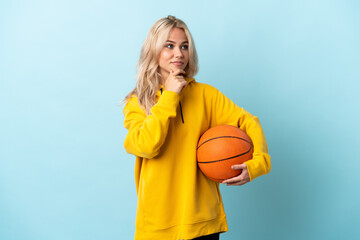 Young Russian woman playing basketball isolated on blue background thinking an idea while looking up