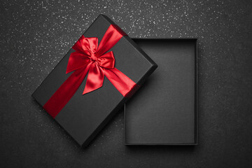 Opened black gift box with a red ribbon and a large bow on a dark granite surface. Empty box. Mockup.