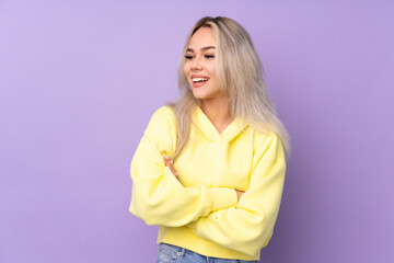 Teenager girl wearing a yellow sweatshirt over isolated purple background happy and smiling