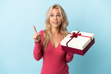 Young Russian woman holding a gift isolated on blue background intending to realizes the solution...