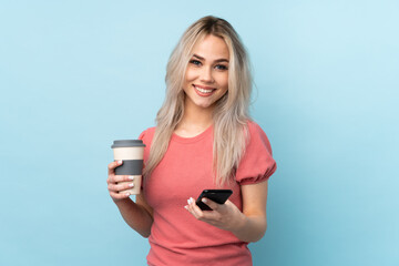 Teenager girl over isolated blue background holding coffee to take away and a mobile