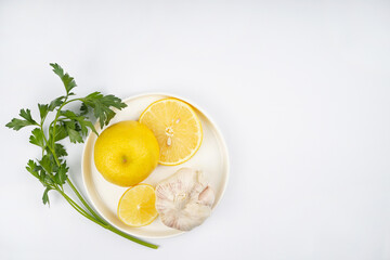 Lemon, garlic, parsley on round plate, white background. Recipe, vitamin, immunity concept. Top view, flat lay, copy space.