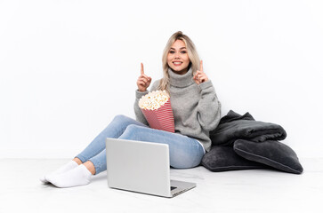 Teenager blonde girl eating popcorn while watching a movie on the laptop pointing up a great idea