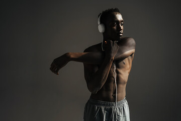 Fototapeta na wymiar African american sportsman using headphones while stretching his arm