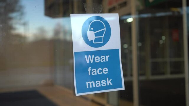 Office worker hangs "Wear face mask" sign on glass door during pandemic covid-19 coronavirus quarantine. Keep yourself and others safety.