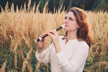 A flute player holds a black flute while standing in the autumn field