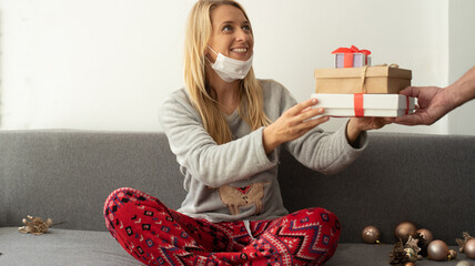 Woman wearing Christmas pajamas get the gift from some man. Blond Female smiling and happy sit on the gray sofa get the small box gift, anticipation of a holiday and a miracle  gift  for new year.