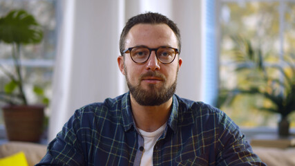 Portrait of handsome bearded man looking at speaking at camera having video call from home