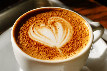 Cup of cappuccino coffee with milk foam and heart on a table in a cafe in the morning