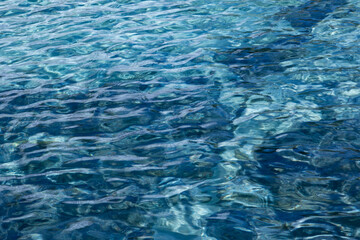 Light and dark blue water in a pool with slightly moving waves and reflections of the sun