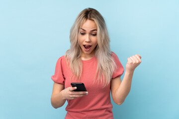 Fototapeta premium Teenager girl over isolated blue background surprised and sending a message