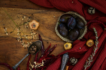Autumn still life . Fresh plums, red fabric and dried herbs on wooden background. 