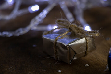 A Christmas gift in silver paper and a Christmas tree toy - a blue ball on a background of white lights.