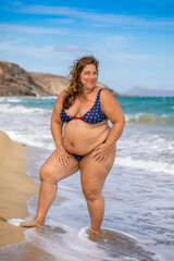 Sehr mollige Frau mittleren Alters mit langen Haaren stehend im Bikini am Strand auf Fuerteventura
