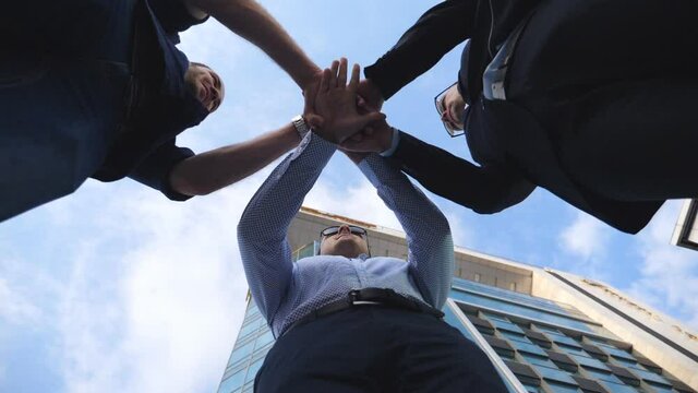 Young business partners standing and stacked hands together outdoor. Successful colleagues holding their arms in centre and falling them down. Unity and teamwork concept. Low angle view Slow motion