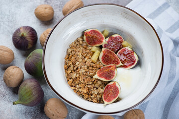White bowl of granola served with fig fruits, greek yogurt and honey, horizontal shot on a beige stone surface