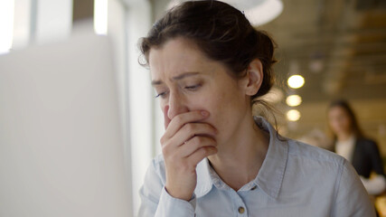 Young sick woman coughing and feeling unwell working with laptop in office