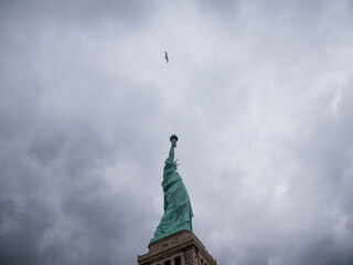 Canted shot of the statue of liberty, seagull flying, grey sky, low angle view