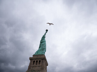 Canted shot of the statue of liberty, seagull flying, grey sky, low angle view