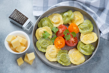 Grey plate with italian ravioli, grated parmesan cheese and sliced tomatoes, studio shot on a light-blue stone background