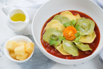 White bowl with ravioli on tomato sauce bedding, grated parmesan cheese and olive oil, studio shot on a white concrete surface