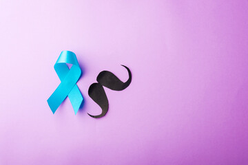 Black mustache paper and light blue ribbon, studio shot isolated on purple background, Prostate cancer awareness month, Fathers day, minimal November moustache concept