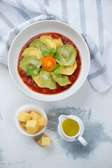 Ravioli with tomato sauce and grated parmesan cheese, above view on a white concrete background, vertical shot