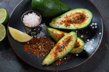 Close-up of sliced avocado with japanese shichimi seasonings and pink salt served on a black plate, studio shot