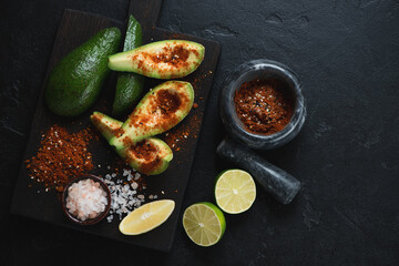 Top view of avocado slices seasoned with shichimi togarashi, salt and lemon, horizontal shot on a black stone background, copyspace