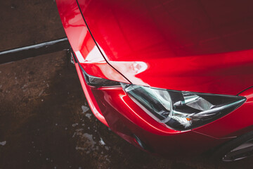Modern red car close up on the headlight, modern sedan vehicle parking on the wet floor.