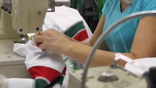 Woman sews hockey team uniform with machine tool in shop