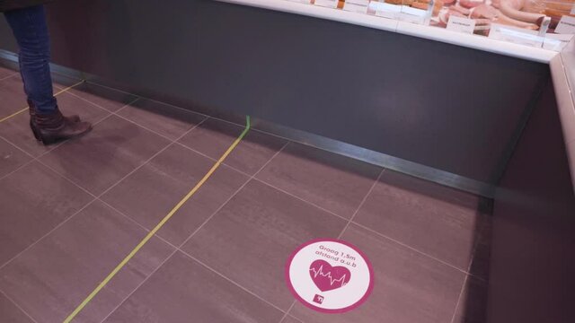 Social distancing sticker signs on a deli floor indicate where a customer should stand