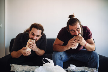 Two friends eating a dürum kebab at home, on the living room while sitting on the sofa