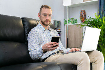 Young man making a call using a smartphone and laptop for work. Concept working home during 2020 covid coronavirus pandemic