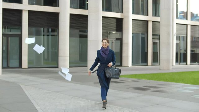 Excited businesswoman walking out business center throwing document away