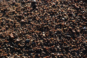 Wet sand and small stones.
In the rays of the setting sun, wet coastal sand in which there are many small pebbles. Pebbles of different shapes and colors. Small stones texture.
