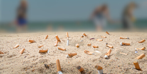 cigarette butts pollute a beach where unrecognizable people go on vacation