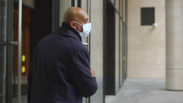 Mature successful businessman leaving office building and removing protective mask