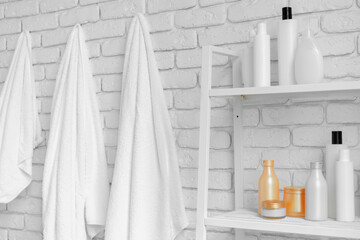 Bathroom shelving with cosmetic bottles and hanging towels against white brick wall