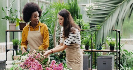 Mixes-races floral store female employees in aprons making bouquets at work. Caucasian and African American women florists working in flower shop together. Business concept