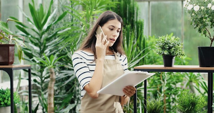 Close up of mixed-races females florists working at floral store. Caucasian woman talking on smartphone in own flower shop. African American woman making bouquet at work. Floristry concept