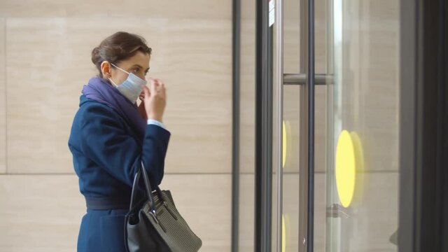 Side view of businesswoman putting on safety mask and entering office building