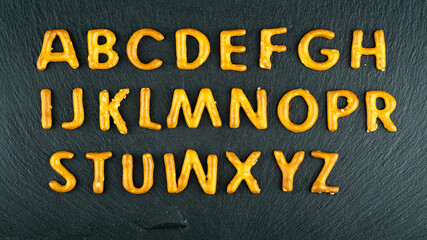 snack alphabet made of salty sticks letters on black stone background. Pretzels, salty snacks text.