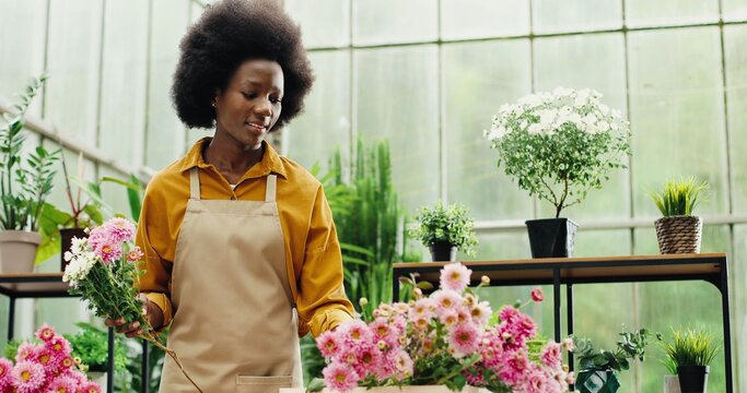 Portrait of African American happy woman flower store manager making bouquet at workplace indoor. Young female florist entrepreneur working with flowers in floral center. Floristry concept